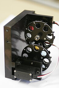 Two filter wheels used in fluorescence microscopy, each containing multiple optical filters inside. These filter wheels allow rapid and precise selection of excitation and emission wavelengths by rotating different filters into the optical path. 