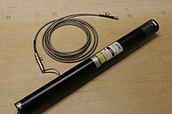 Photograph of a Helium-Neon laser tube with its optical fiber. The label on the tube displays manufacturer information and specifications. 